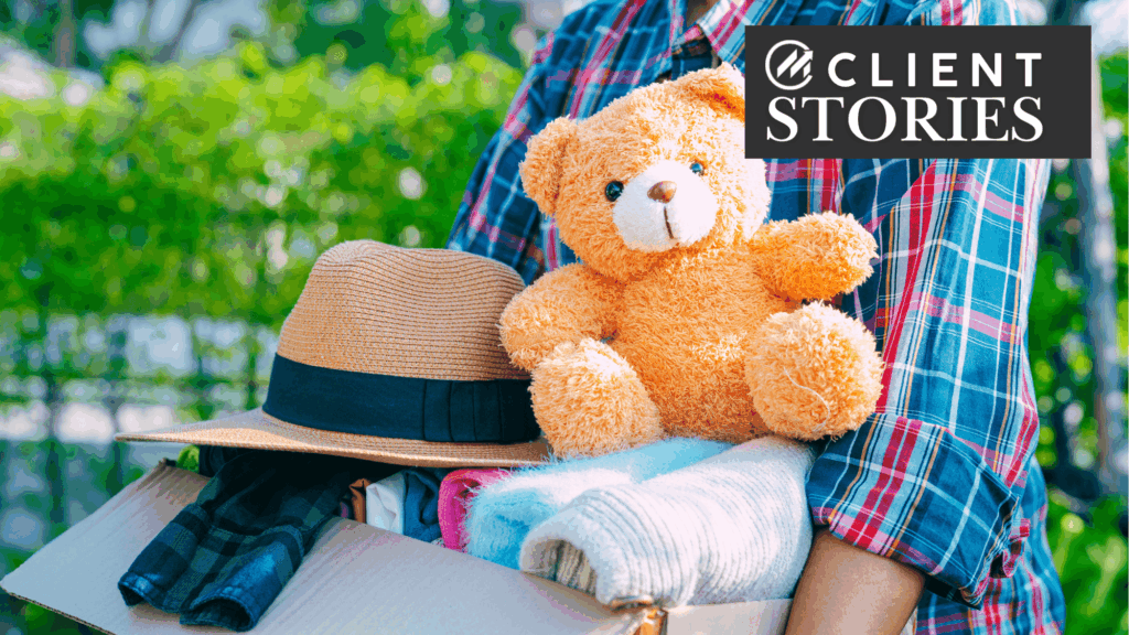 Person carrying a box of clothes and a teddy bear.