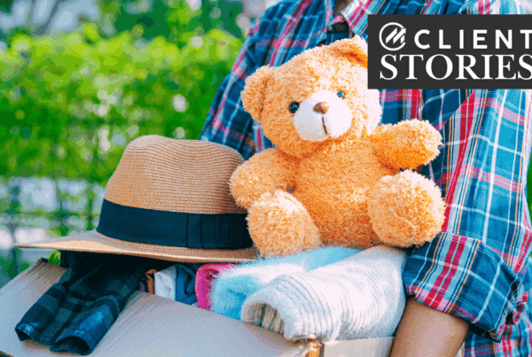 Person carrying a box of clothes and a teddy bear.